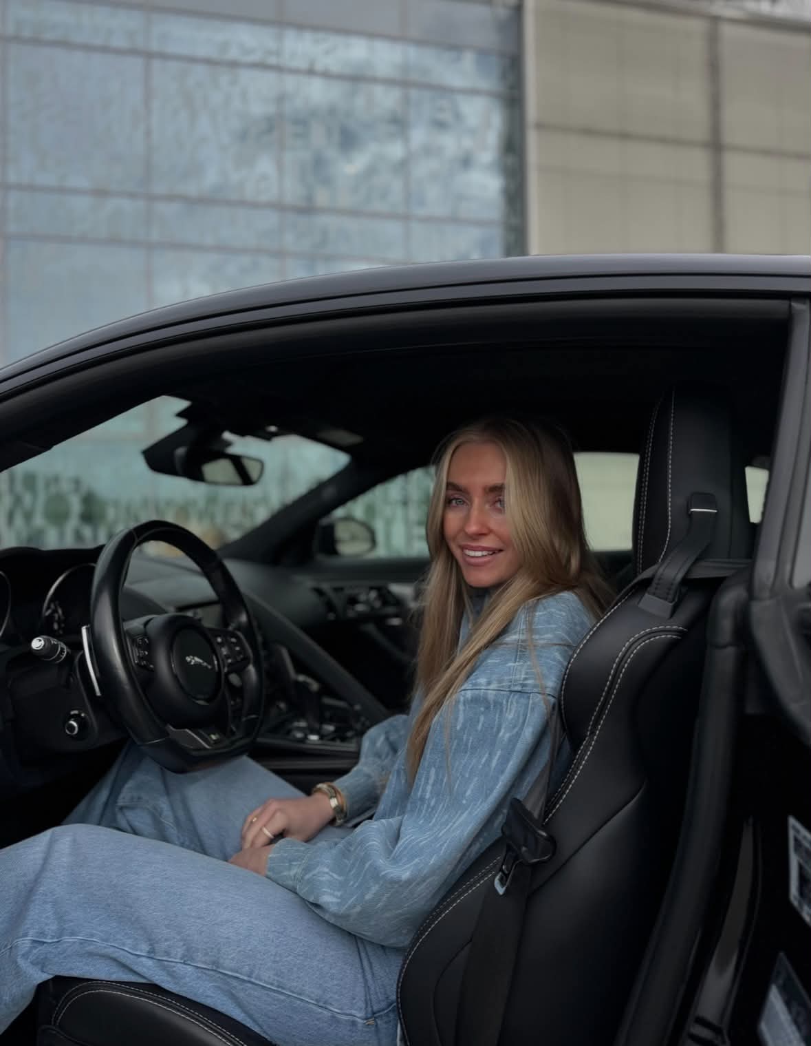 Charlotte smiler fra førersetet i en svart sportsbil